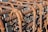 A close-up view of a grid structure made from rusted steel rebar, with each bar intricately twisted and held together by looping wire ties. The rusty texture and patina are clearly visible, indicating weathering and age.