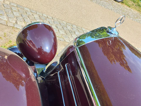 A skilled mechanic polishing the chrome details on a classic Mercedes-Benz hood.
