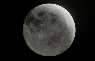 A detailed view of the moon, showcasing its cratered surface in a monochromatic grayscale. The contrast highlights various lunar features including dark maria and lighter highlands.