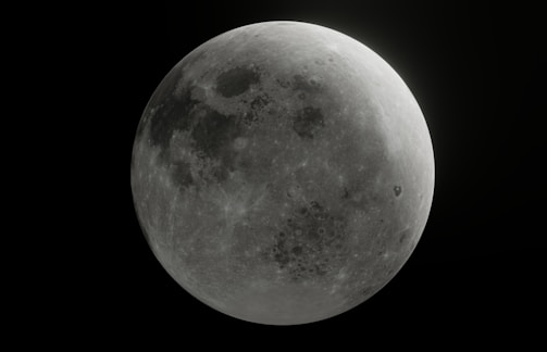 A detailed view of the moon, showcasing its cratered surface in a monochromatic grayscale. The contrast highlights various lunar features including dark maria and lighter highlands.