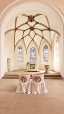 A serene wedding altar adorned with white and gold decorations, softly lit by natural light through stained glass.