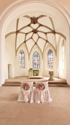 A serene wedding altar adorned with white and gold decorations, softly lit by natural light through stained glass.
