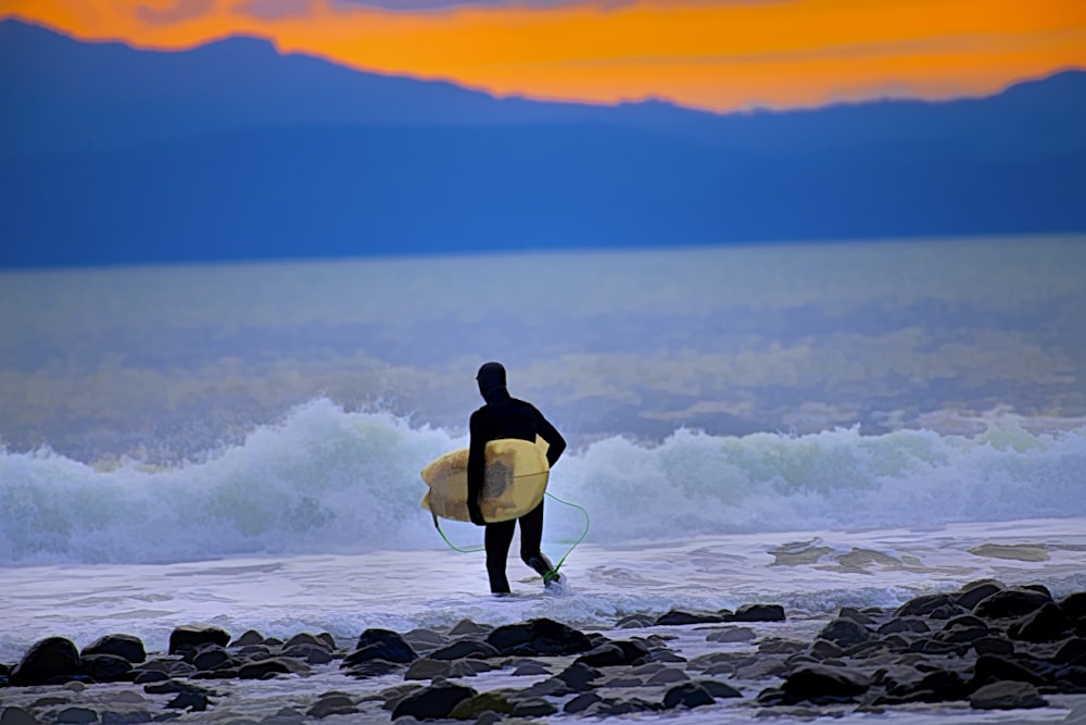 a man holding a surfboard while standing on a rocky beach
