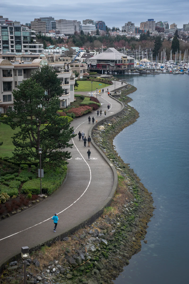 People walking and running along the curving False Creek seawall in Vancouver beside a marina