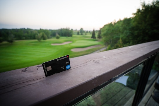 A credit card with Aeroplan branding is placed on a wooden railing, overlooking a lush green golf course. The scene includes well-maintained grassy areas, trees, and a soft, serene sky in the background.