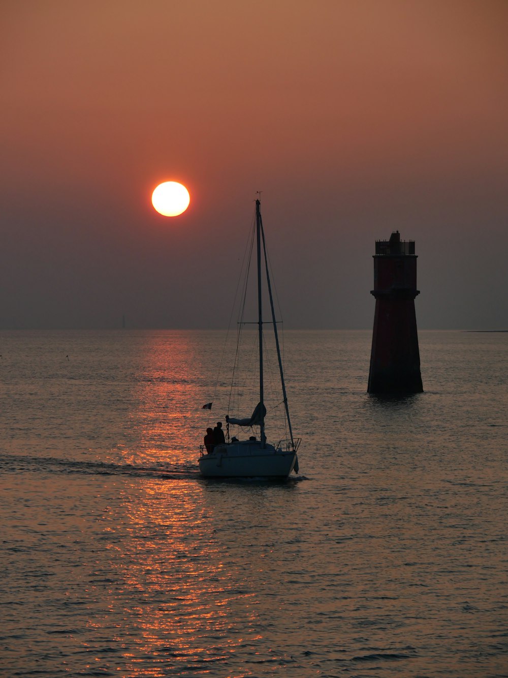 a sailboat in the water with a lighthouse in the background