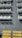 Rows of white benches casting distinct shadows on a gray, textured surface. The benches are arranged in orderly lines, suggesting a seating area. Bright yellow non-slip strips mark steps at the bottom of the image.