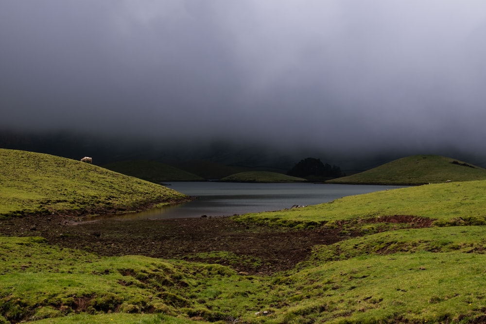 a lake surrounded by lush green hills under a cloudy sky