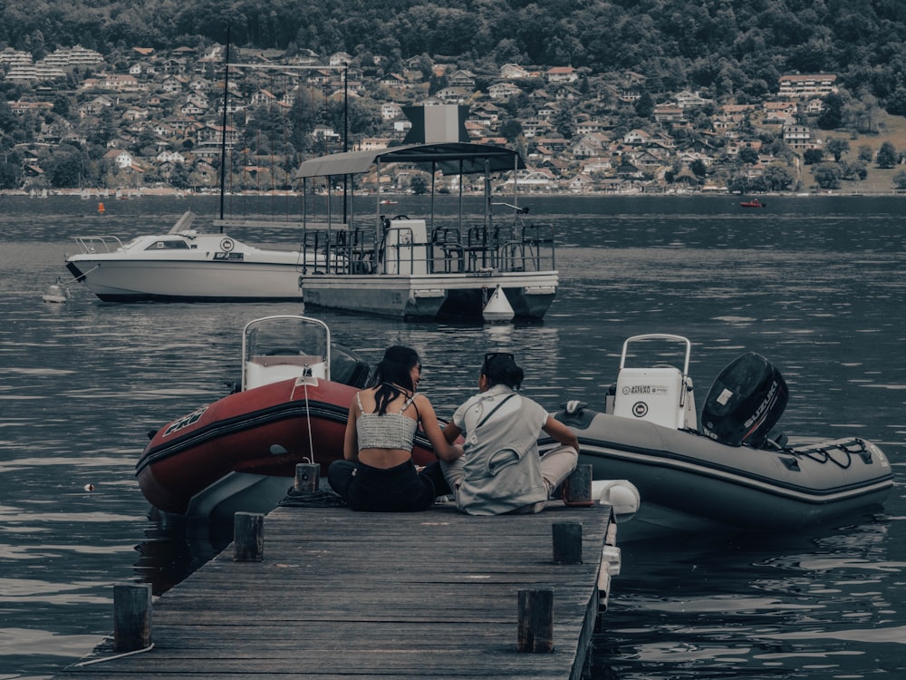 two people sitting on a dock next to a boat