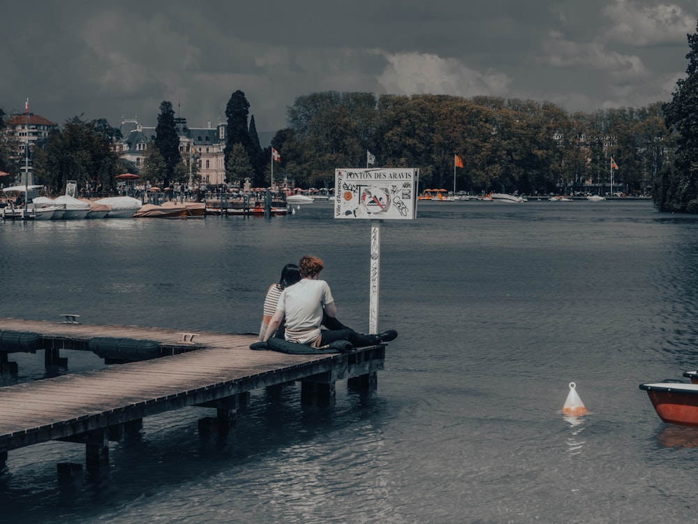 a man sitting on a dock next to a body of water