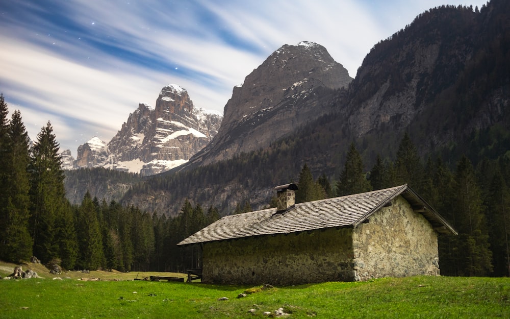 a small house in a field with mountains in the background