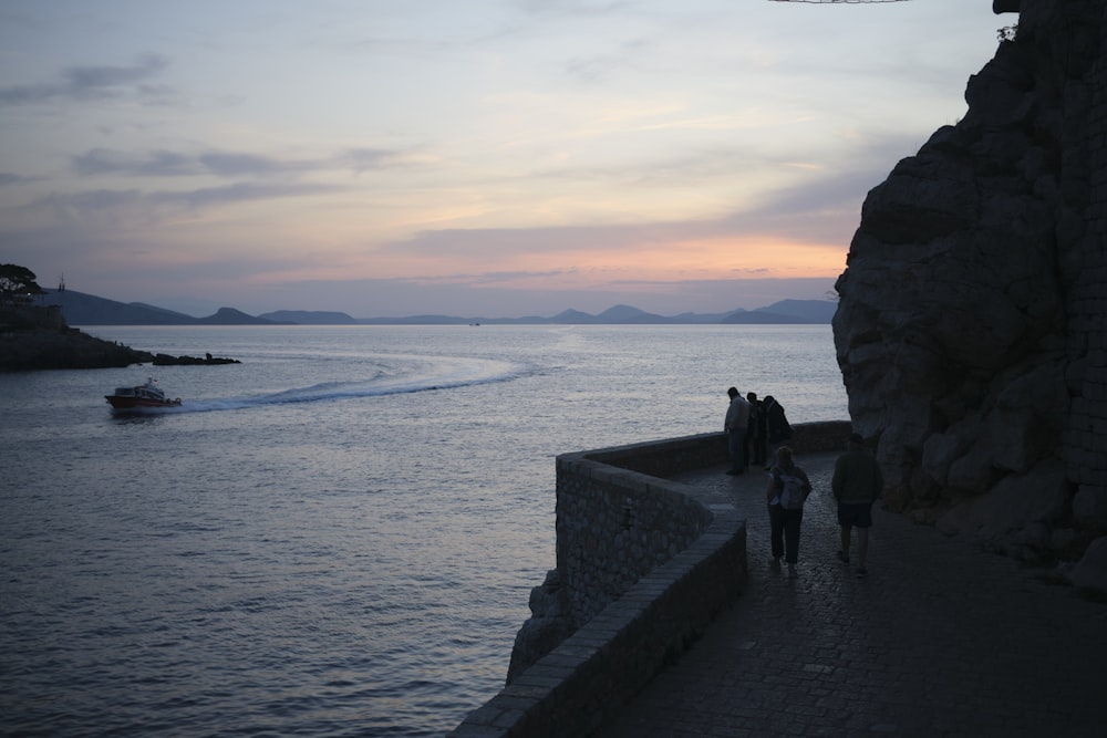 a group of people walking along a stone wall next to a body of water