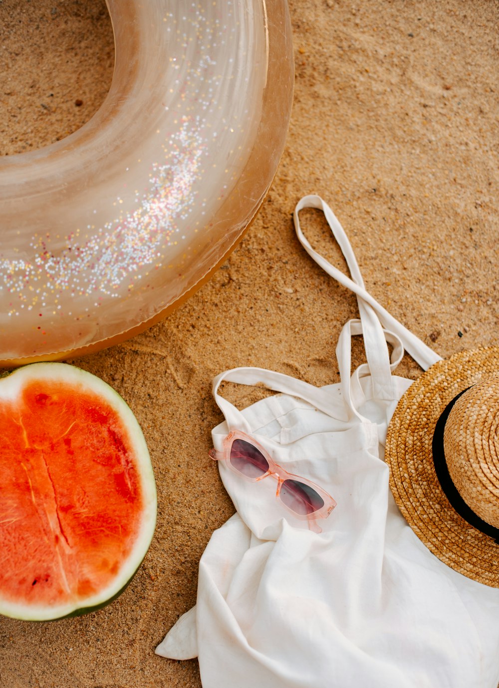 a watermelon and a straw hat on a beach