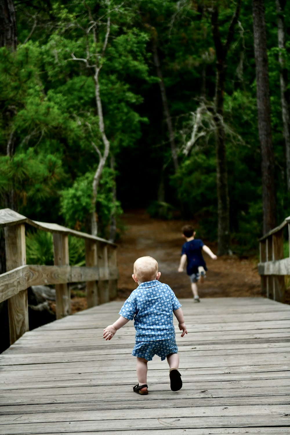 a little boy running across a wooden bridge