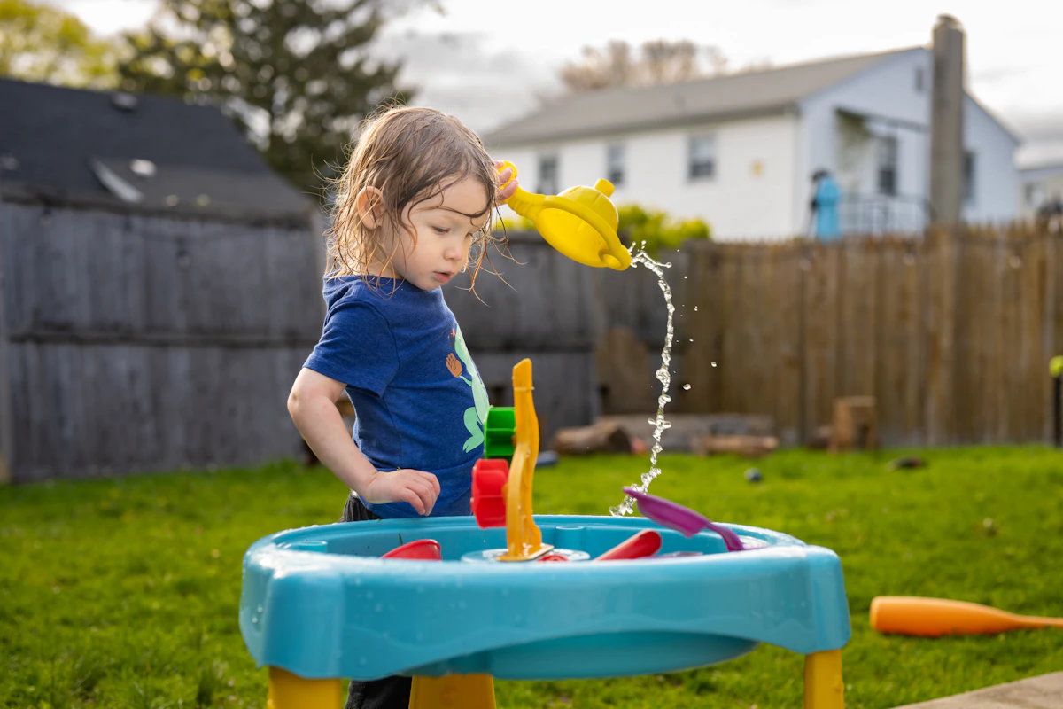 Toddler standing at an outdoor water table, splashing and pouring