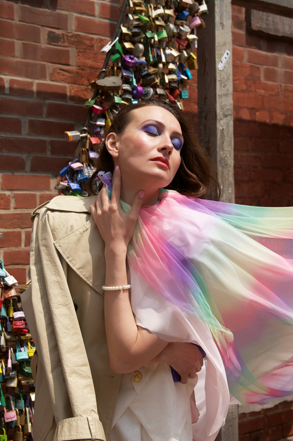 a woman holding a colorful scarf in front of a brick wall