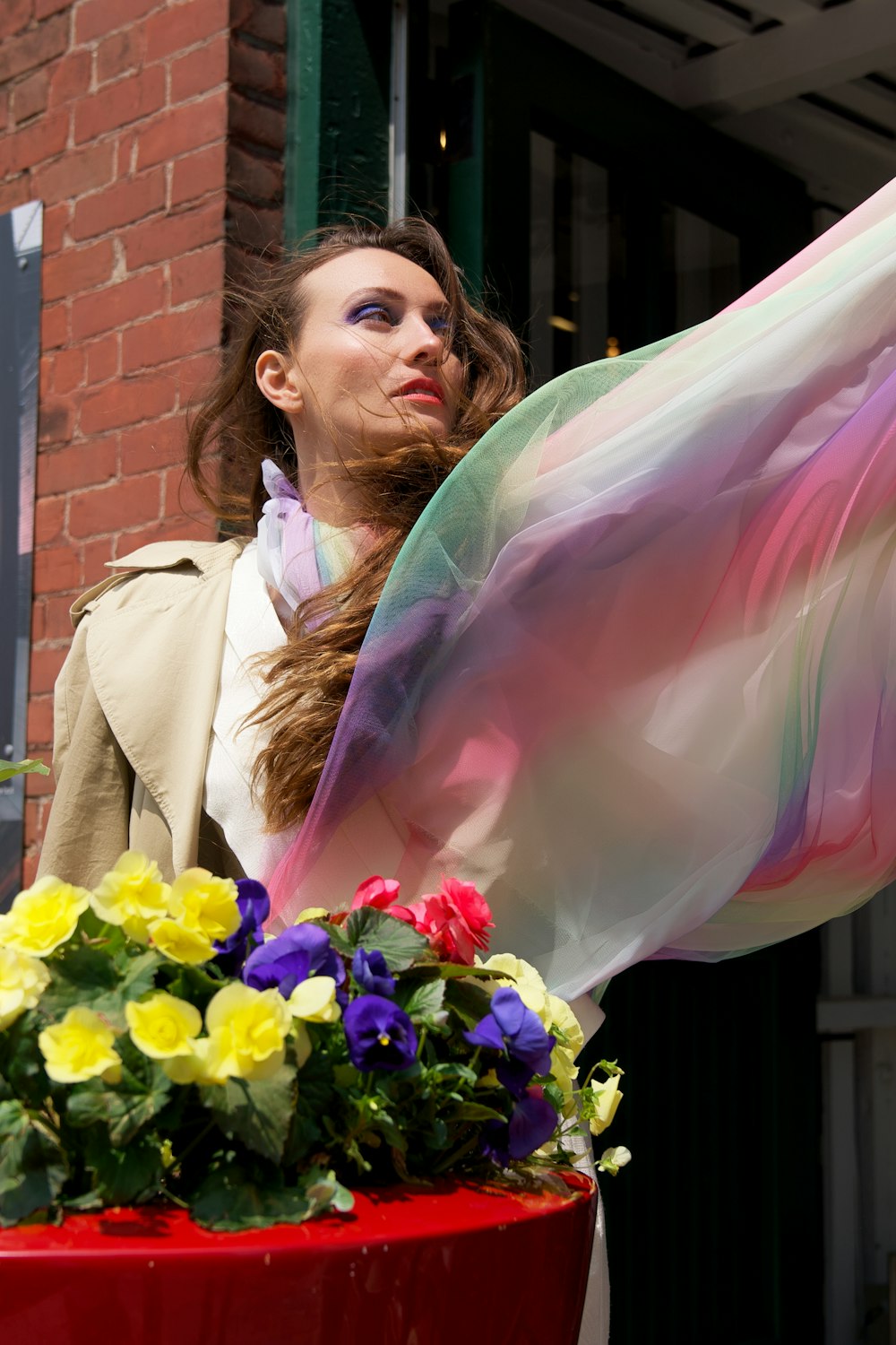 a woman standing next to a flower pot holding a scarf