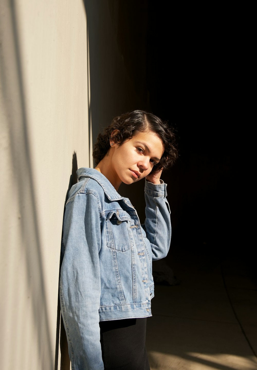 a woman in a jean jacket leaning against a wall