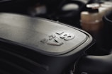 A close-up view of a 5.7L V8 engine cover with bold lettering. The metallic surface has a textured finish, and the background shows parts of the engine compartment.