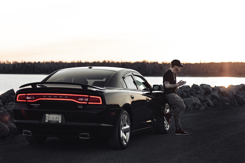 a man standing next to a black car near a body of water