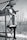 A person in athletic attire is climbing a metal structure outdoors. The background consists of bare trees, suggesting a winter or early spring setting. The individual is wearing a cap and sports shoes, indicating they might be engaging in an outdoor exercise or adventure activity.