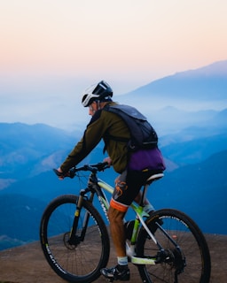 A cyclist riding a mountain bike on a rugged trail with Patagonian mountains in the background under warm sunset light.