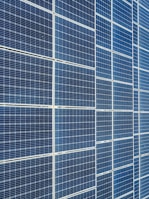 A large array of solar panels with a grid pattern, featuring dark blue and reflective surfaces aligned in a structured manner. The panels are arranged side by side, creating a uniform and organized layout.