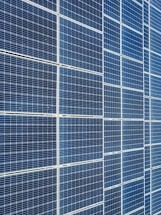 A large array of solar panels with a grid pattern, featuring dark blue and reflective surfaces aligned in a structured manner. The panels are arranged side by side, creating a uniform and organized layout.