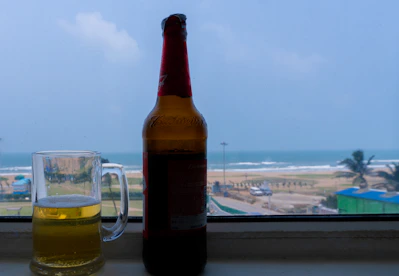 Golden clear hop lager beer bottle with condensation on a sunny beach background