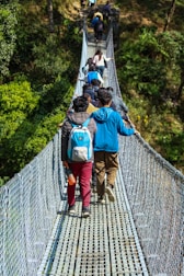 A group of trekkers crossing a wooden bridge near Senaru waterfalls surrounded by tropical greenery.