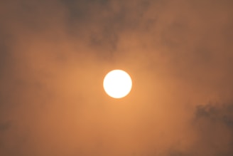 A bright sun is positioned in the center of the image, surrounded by a dense layer of clouds. The atmosphere appears hazy with a warm, orange glow enveloping the scene.