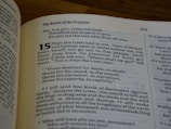 A close-up of an open book showing a religious text with the title 'The Books of the Prophets' and numbered verses. The text is in black on cream-colored pages with some words highlighted in bold.