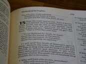 A close-up of an open book showing a religious text with the title 'The Books of the Prophets' and numbered verses. The text is in black on cream-colored pages with some words highlighted in bold.