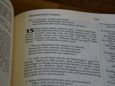 A close-up of an open book showing a religious text with the title 'The Books of the Prophets' and numbered verses. The text is in black on cream-colored pages with some words highlighted in bold.