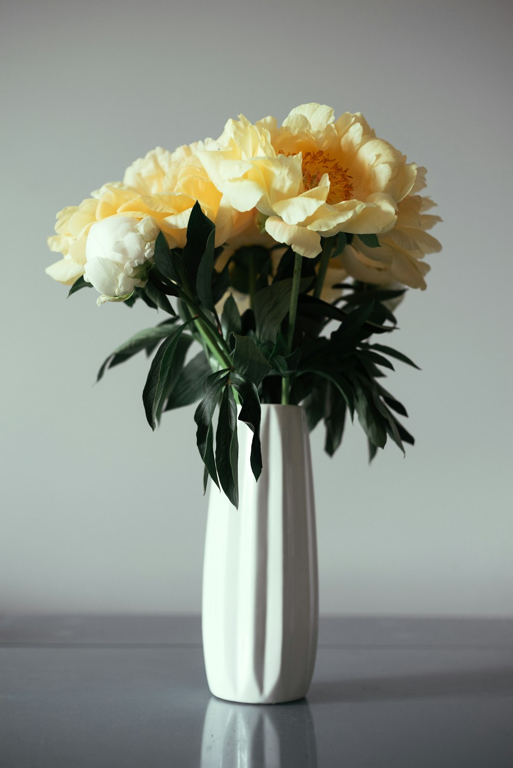 eine weiße Vase, gefüllt mit gelben und weißen Blumen