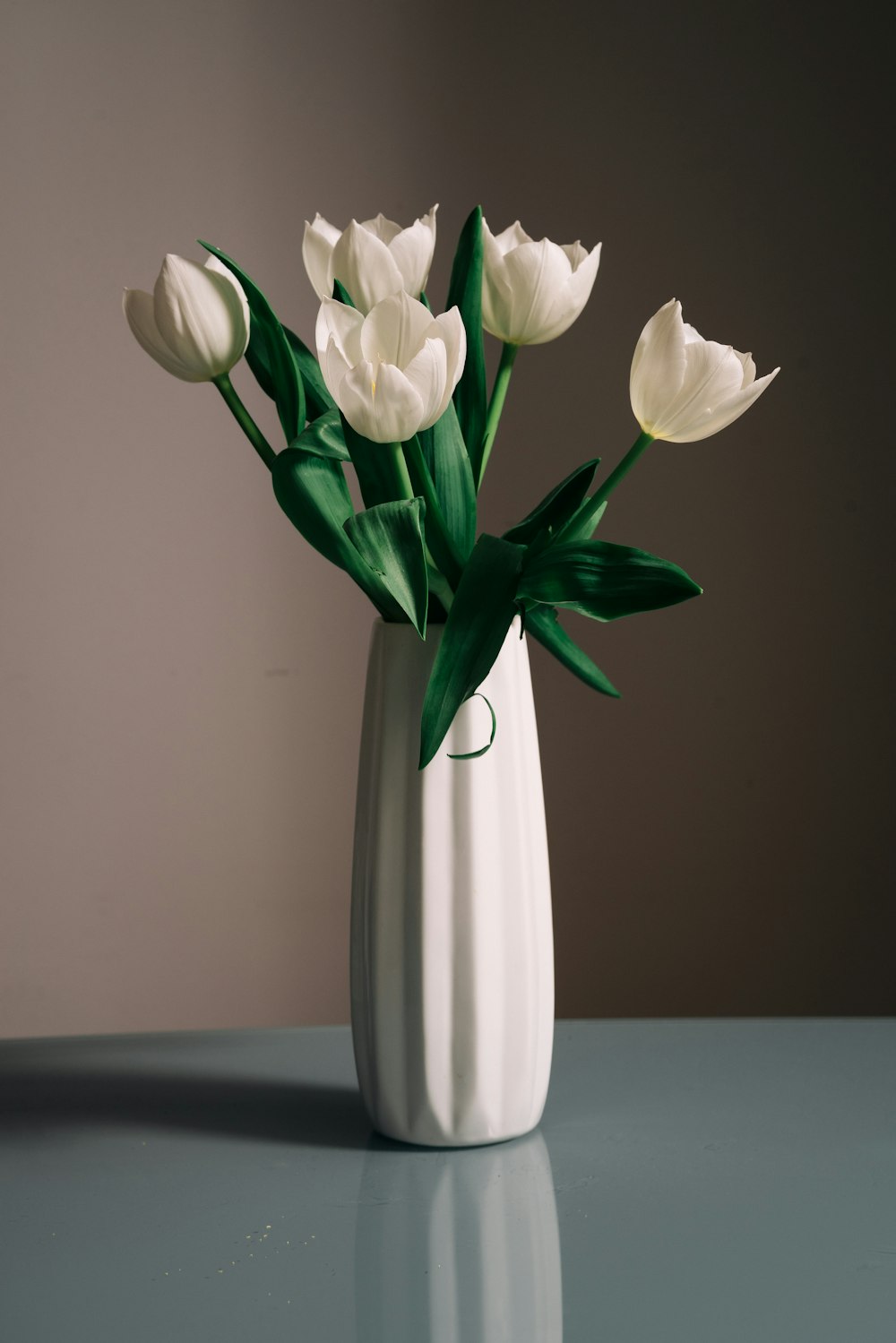 un vaso bianco pieno di fiori bianchi in cima a un tavolo