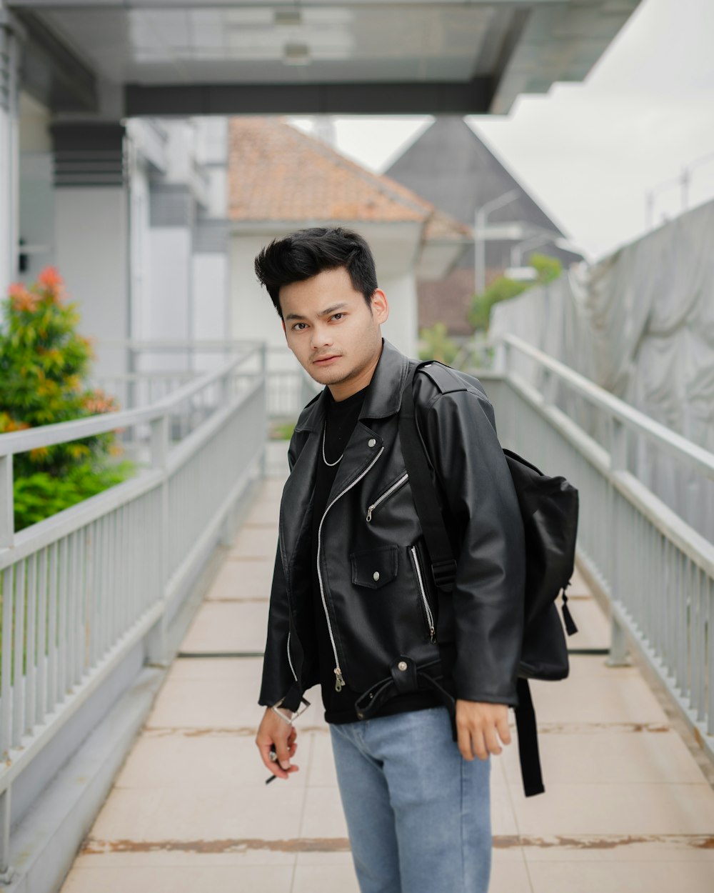 a man in a black jacket and jeans is standing on a bridge