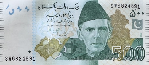 A 500 currency note featuring a portrait of a man wearing a traditional cap. The note includes text in a foreign script, intricate geometric patterns, and a crescent and star emblem. The serial number is visible at the upper right and lower left corners.