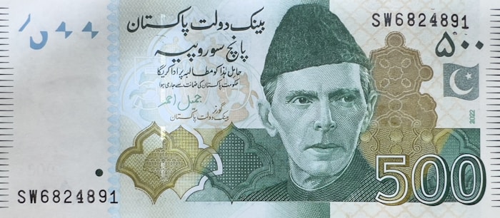 A 500 currency note featuring a portrait of a man wearing a traditional cap. The note includes text in a foreign script, intricate geometric patterns, and a crescent and star emblem. The serial number is visible at the upper right and lower left corners.