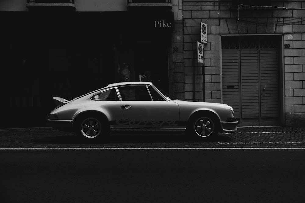 a black and white photo of a car parked in front of a building