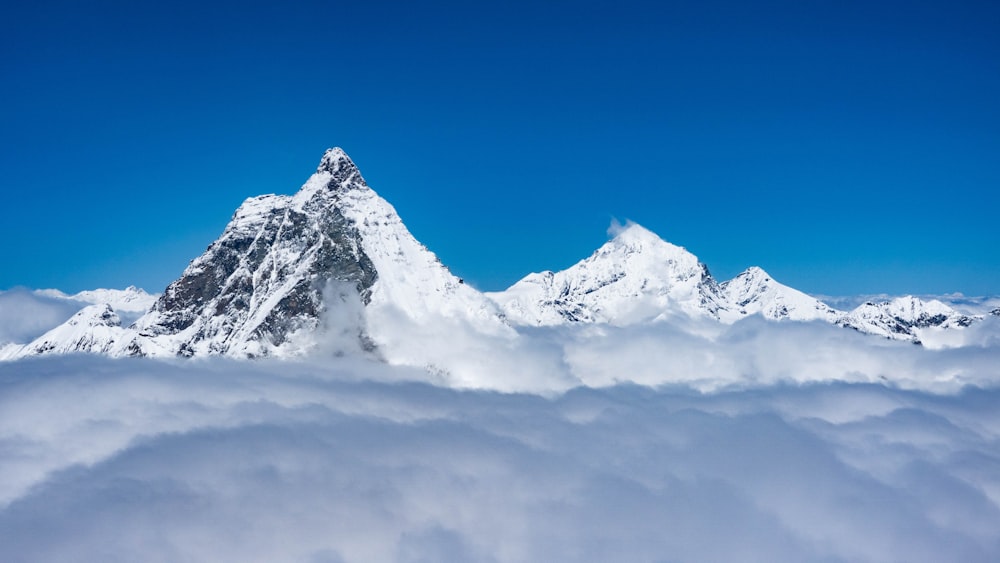 a snow covered mountain in the middle of a cloud filled sky