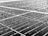Close-up of a solar panel surface covered in numerous raindrops. The texture is visible, with droplets of varying sizes reflecting light. The panel is composed of multiple cells with visible grid lines that create a geometric pattern across the surface.
