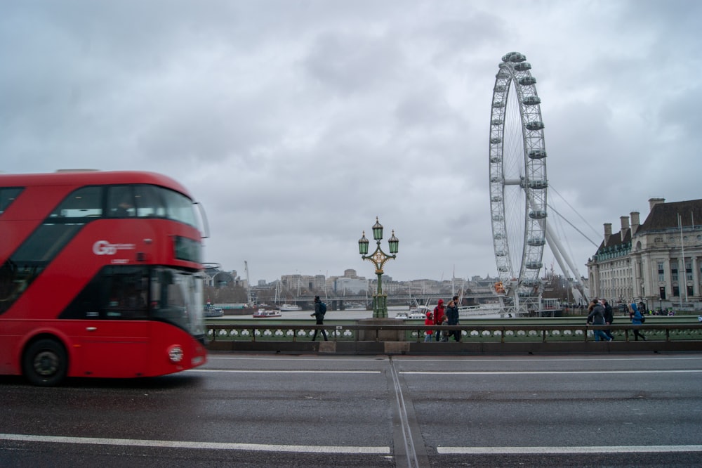 a red double decker bus driving past a ferris wheel