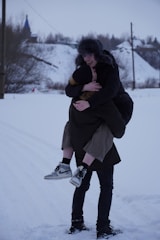 A cheerful helper carrying kids' ski boots and helmets across a snowy ski resort pathway.
