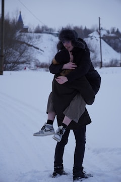 A smiling family ski sherpa carrying multiple pairs of skis and boots through fresh snow.