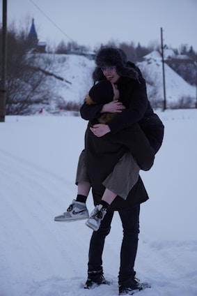 A cheerful helper carrying kids' ski boots and helmets across a snowy ski resort pathway.