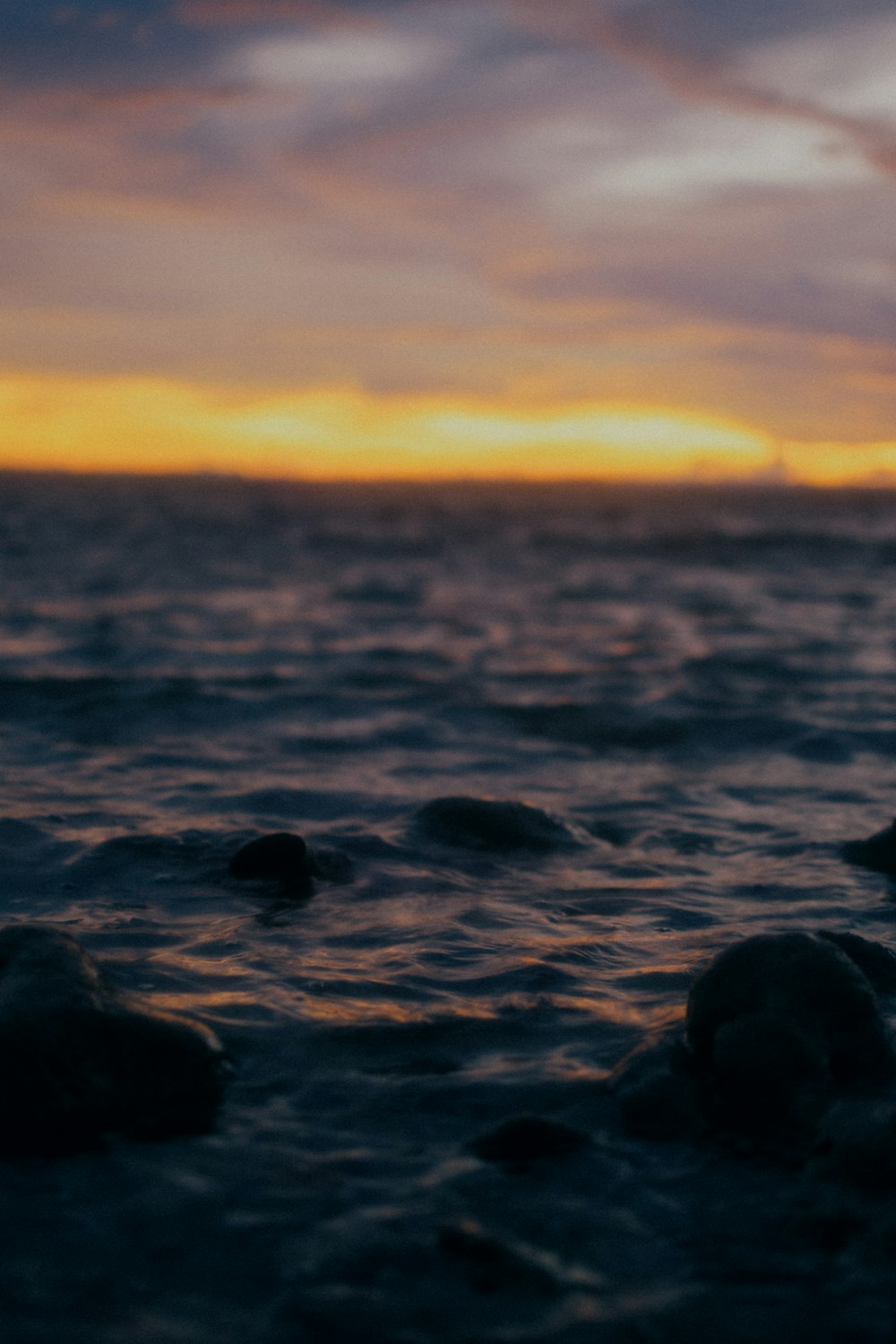 the sun is setting over the ocean with rocks in the foreground