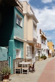 Soft pastel-colored Mediterranean houses lining a narrow street under a clear sky.
