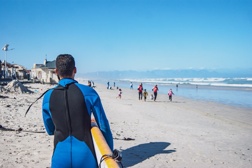 a man in a wet suit carrying a surfboard on a beach