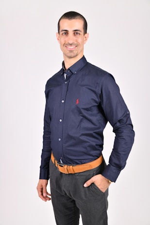 Man wearing a navy polo shirt standing confidently against a minimalist white background.